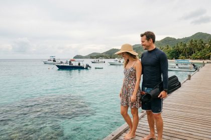 Couple sur un ponton tropical, l'homme équipé de palmes de plongée et la femme en robe regardant la mer turquoise ensemble